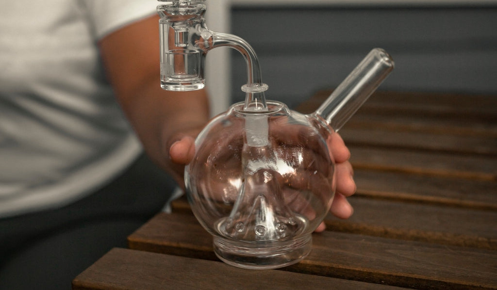 A person holding a glass dab rig on a table