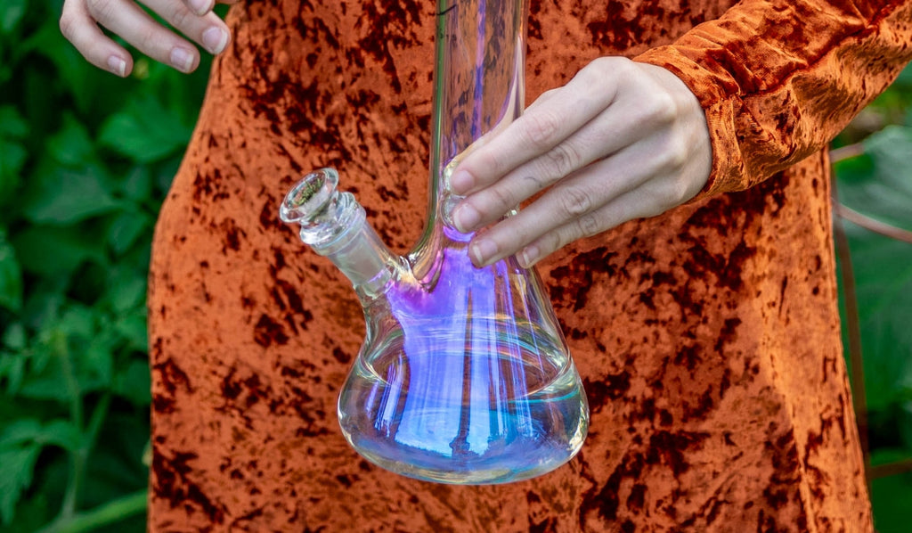Person holding a glass beaker bong with one hand