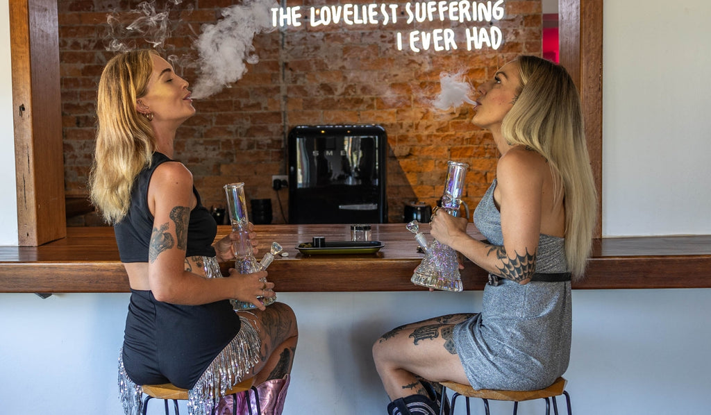 Two women sitting and smoking glass bongs