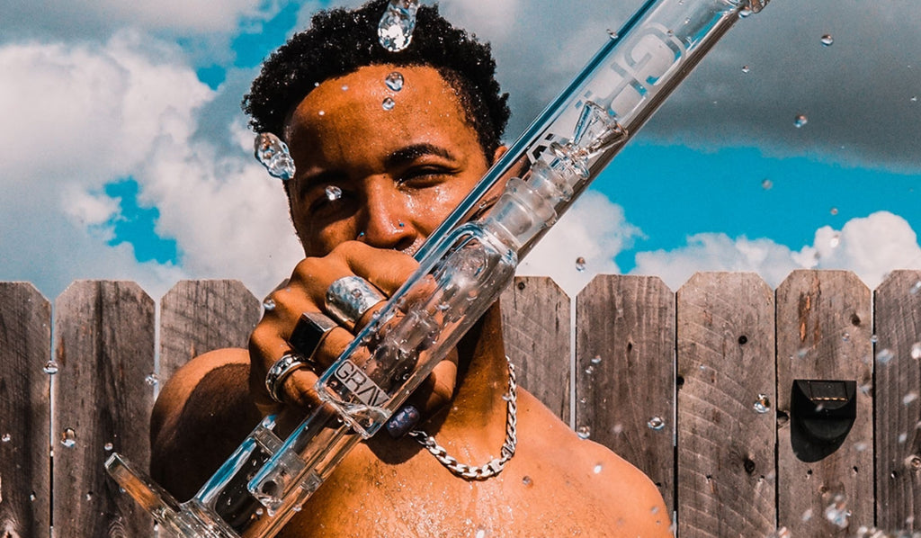 A man holding a glass straight tube bong