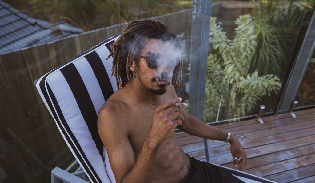 A man sitting on a chair exhaling cannabis smoke