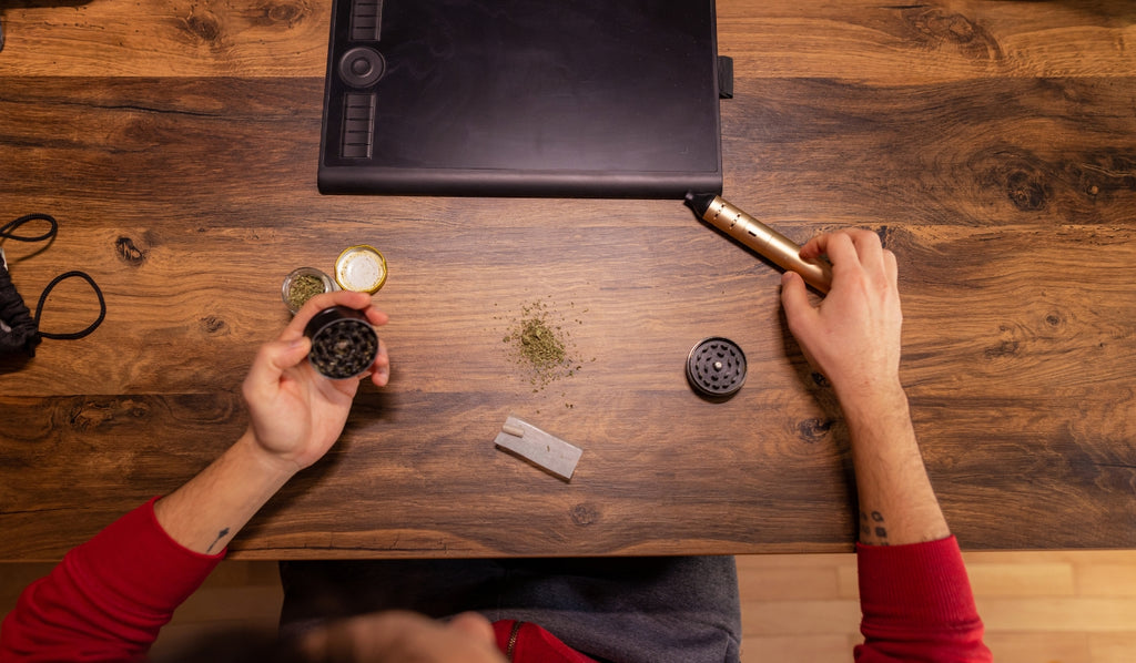A person at a desk preparing a joint with a weed grinder
