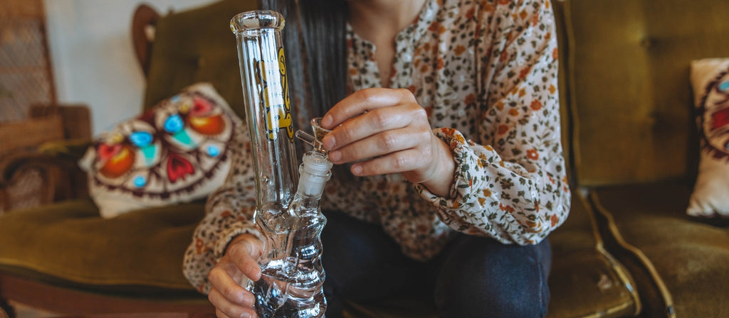 A person packing a glass bong with cannabis