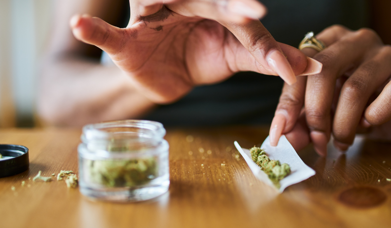 A person rolling a joint next to an open jar of cannabis