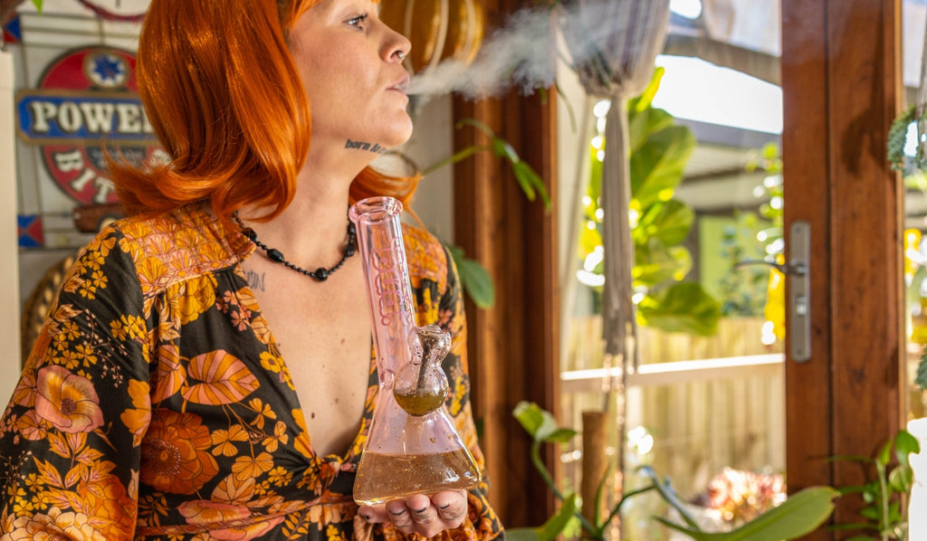 A woman exhaling from a glass beaker bong