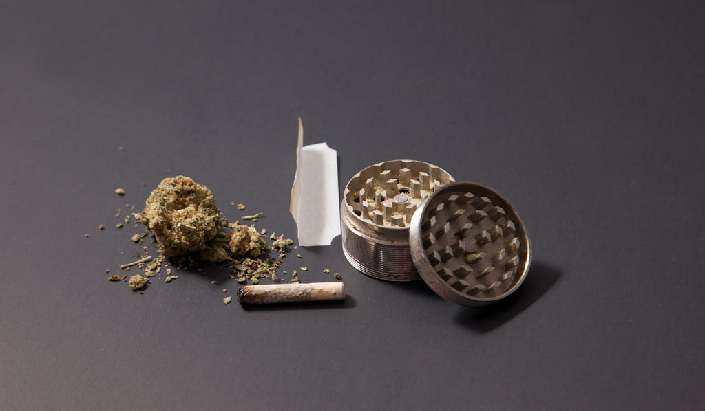 An open weed grinder next to a cannabis bud and a used joint