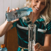 Woman pouring bong water alternative into a glass bong