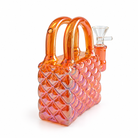 An iridescent orange glass water pipe shaped like a purse, featuring a quilted diamond pattern on the body, dual curved handles, and a clear glass mouthpiece on the side, set against a plain white background.