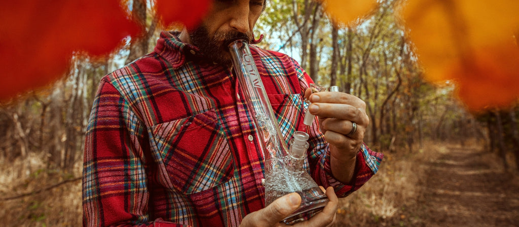 Man in the woods smoking from a glass bong
