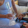 A person about to pack a glass bong with ground cannabis