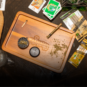 A spread of smoking accessories on a table including a rolling tray, grinder, pre-rolled cones and cannabis