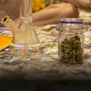 A glass swing top jar filled with cannabis buds and a glass beaker bong