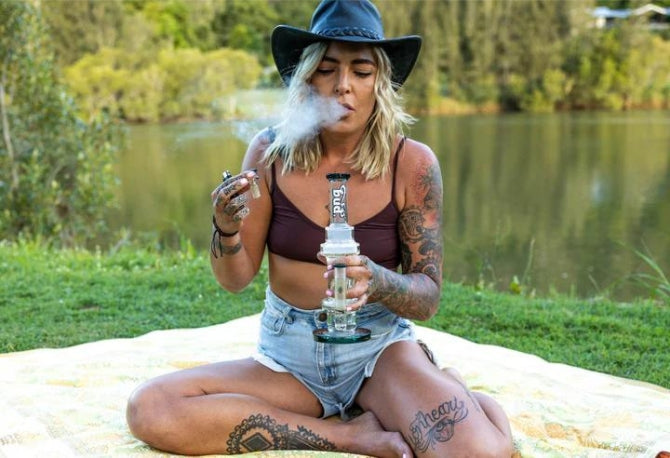 Woman sitting at a park smoking from a Bud Twisted Inline Percolator Bong