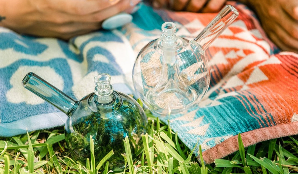 Two glass bubbler bongs on a picnic rug