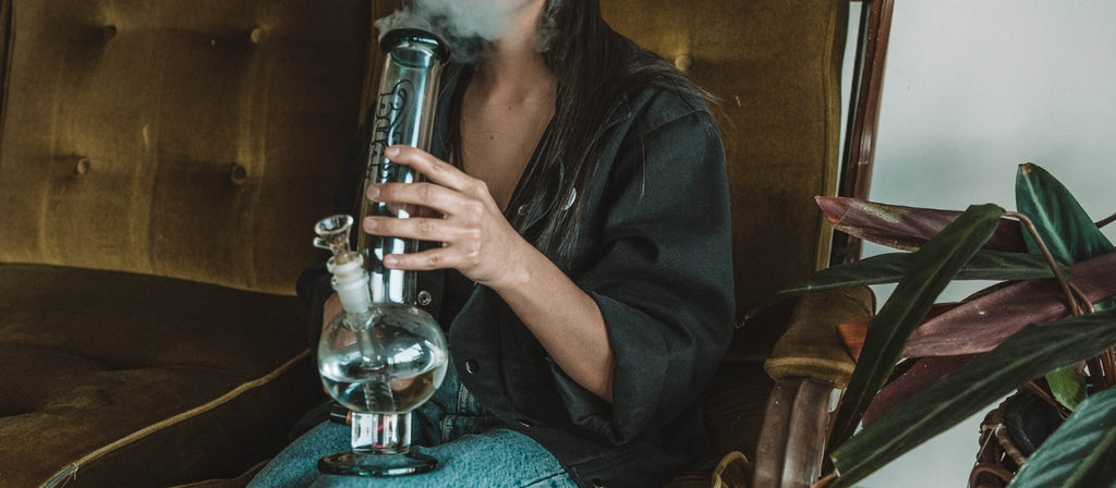 Woman exhaling from glass round base bong